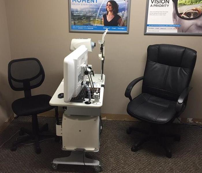 An office with 2 desk chairs and a small desk in between with a computer and eye exam machine
