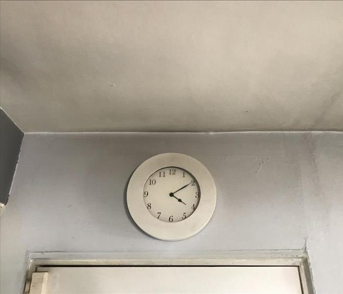 a white clock on a grey wall and a white ceiling with smoke damage